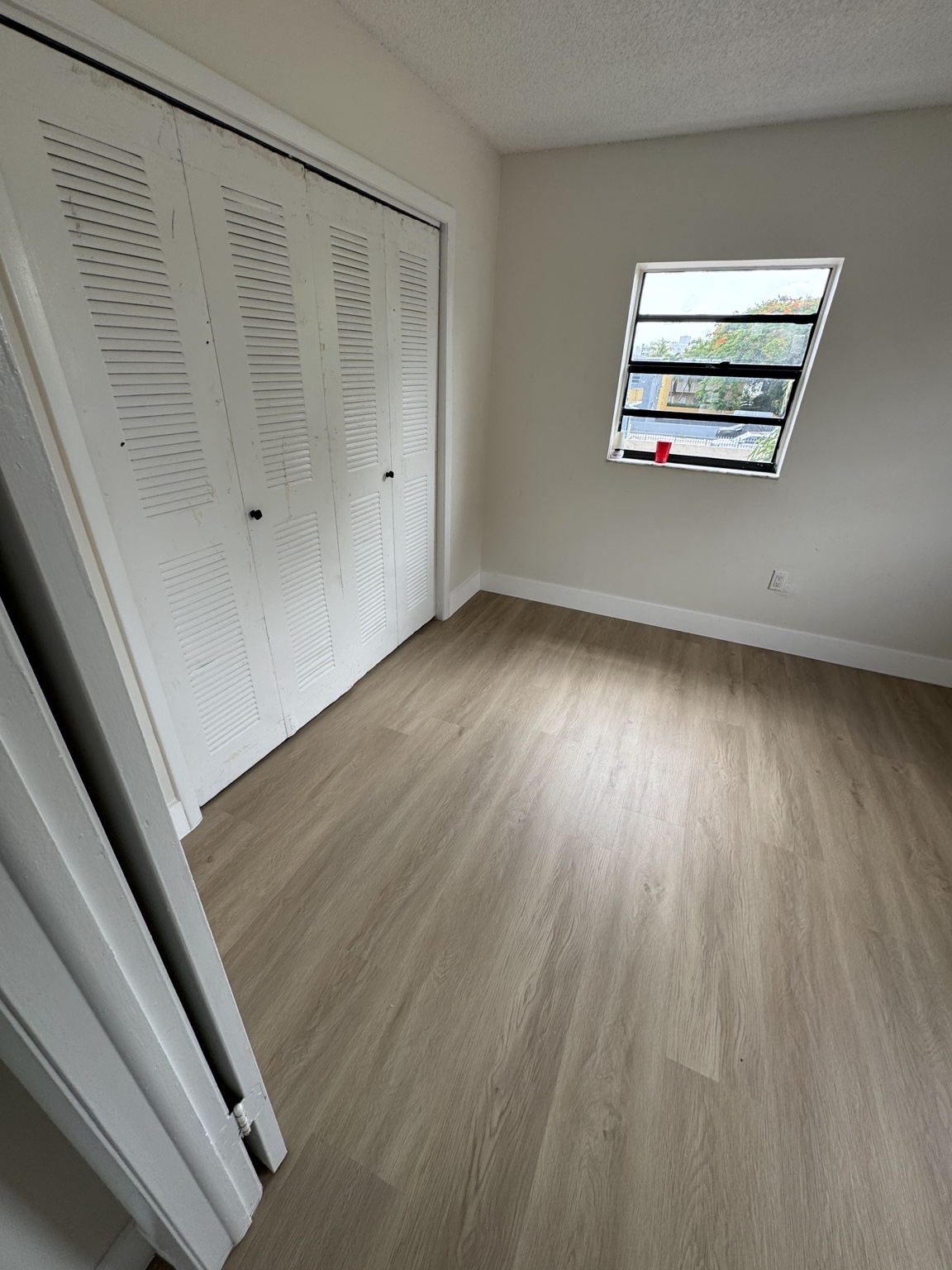 Secondary bedroom finished with light wood-look waterproof vinyl flooring and white baseboards.