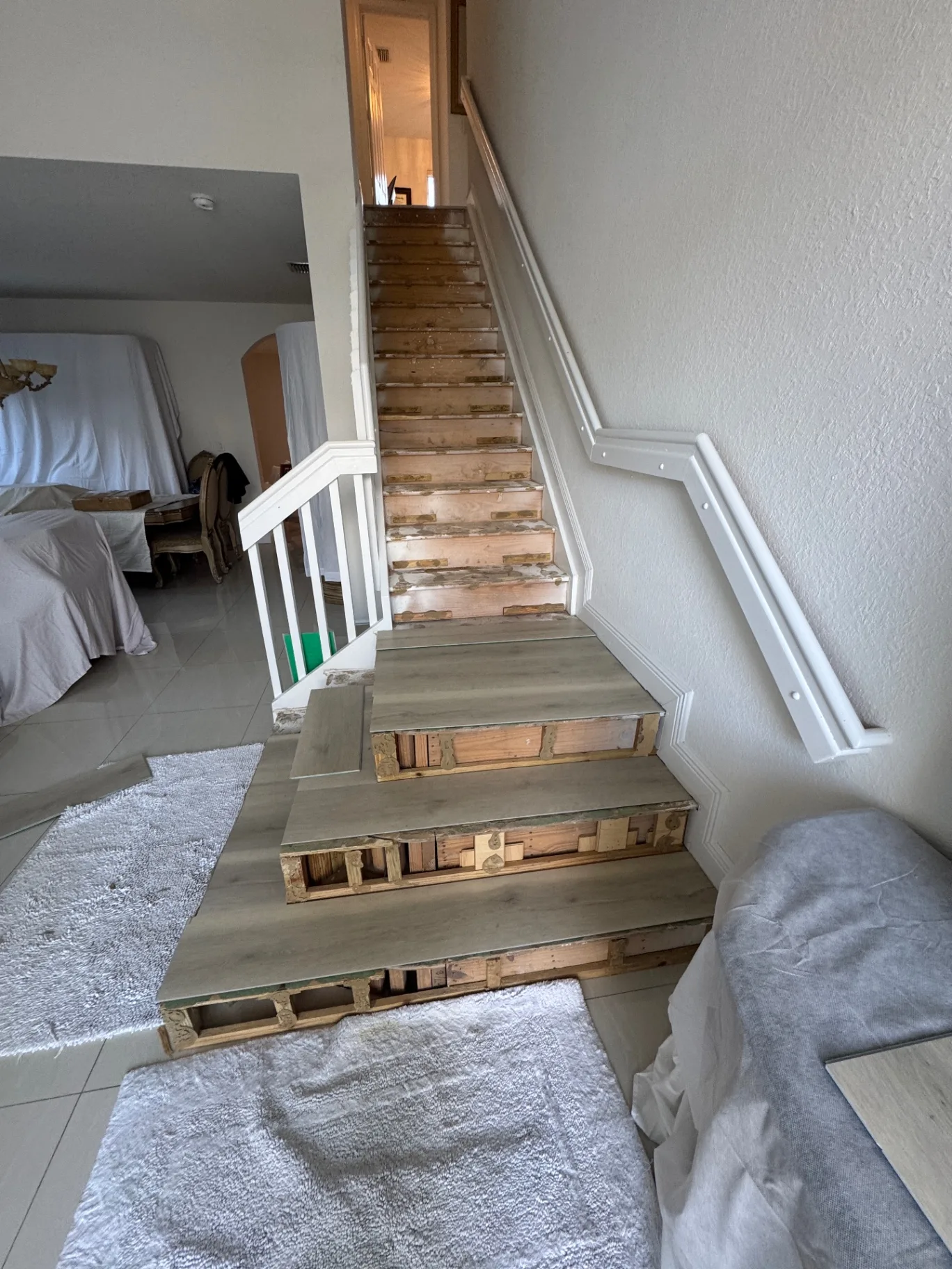 Staircase during installation — new light gray wood-look treads placed on the lower steps, upper steps still bare.