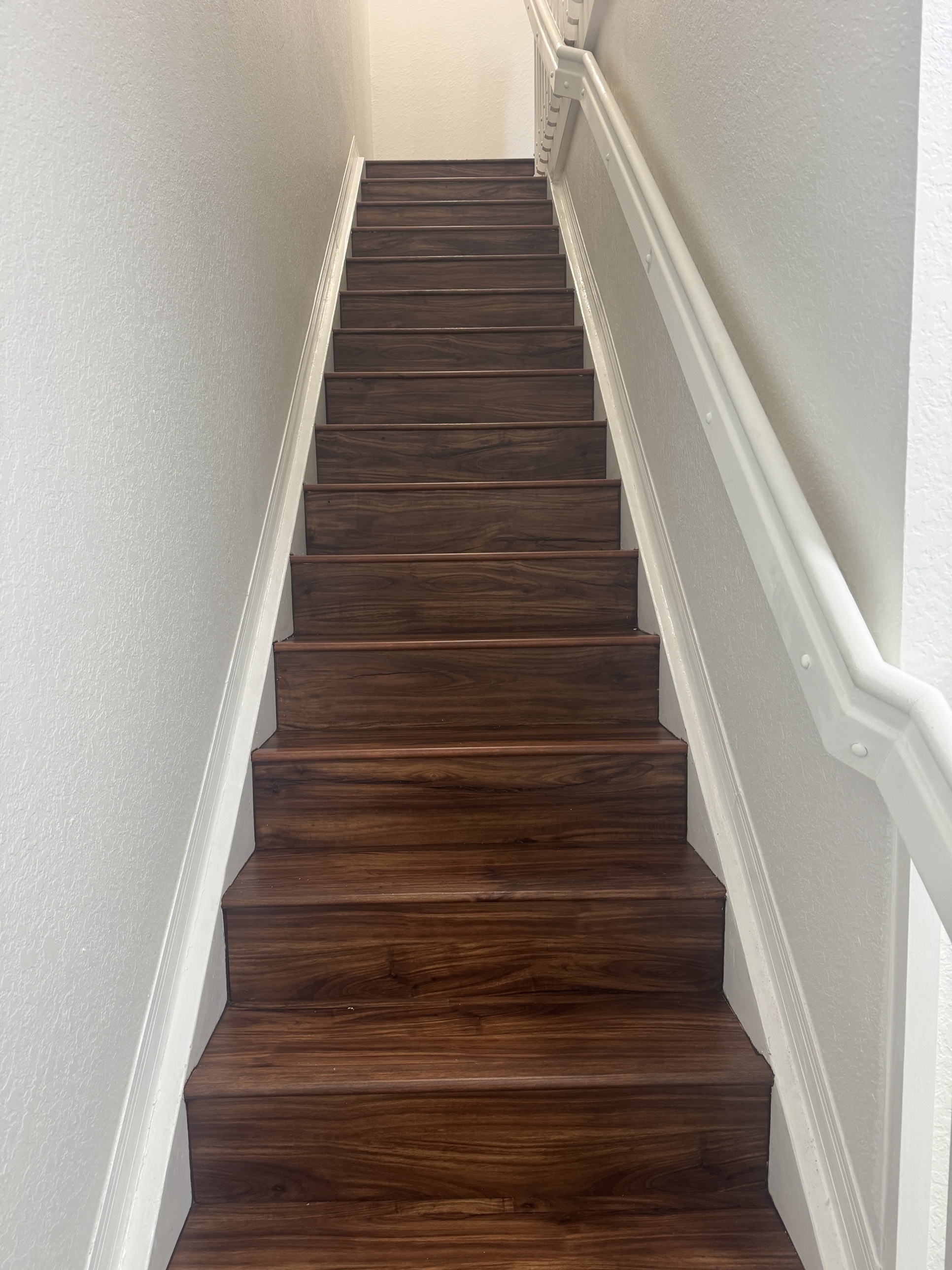 Staircase before new flooring installation showing dark wood treads and risers, shot looking straight up the stairs