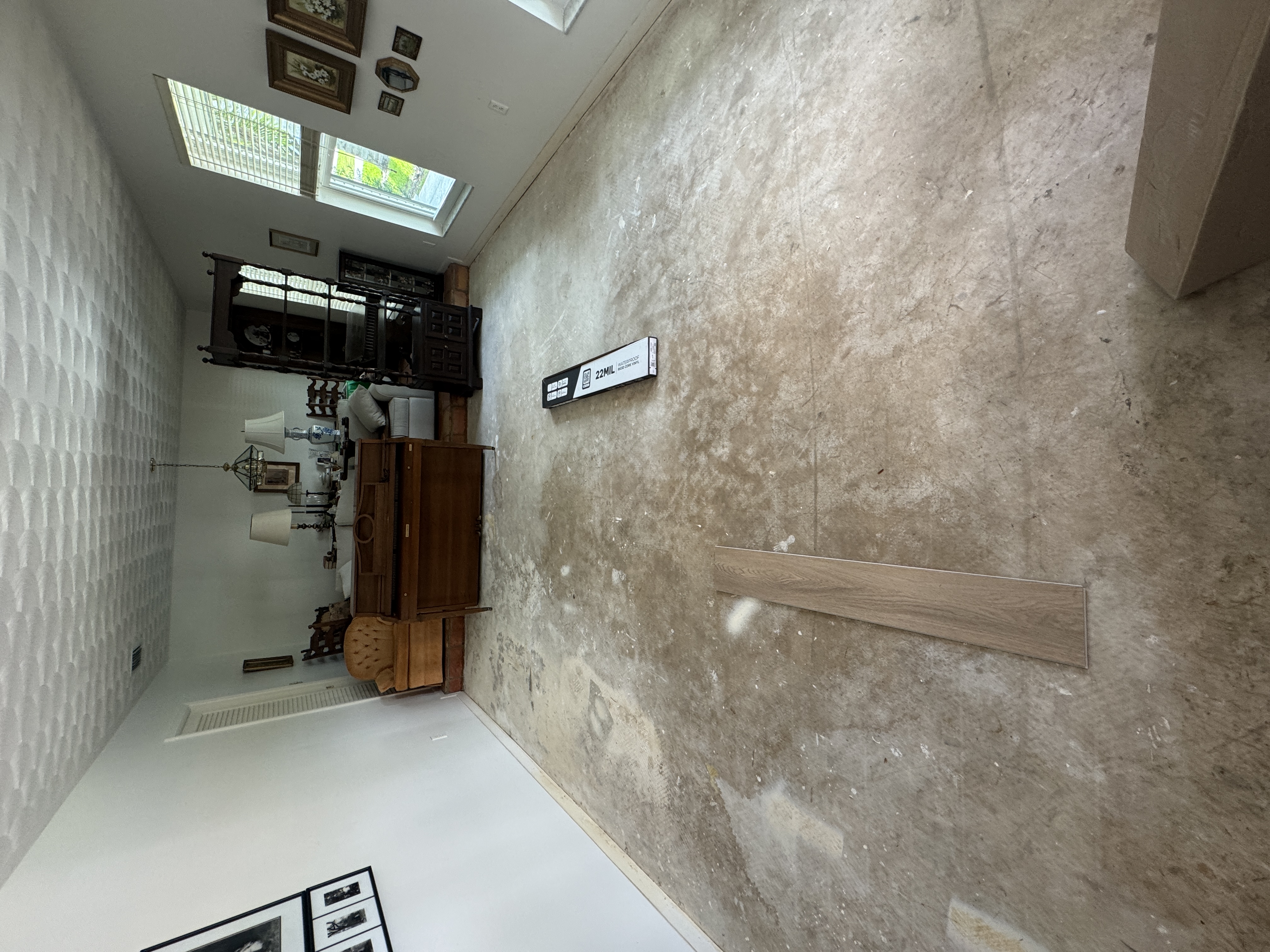 Bare concrete subfloor before vinyl flooring installation in a Coral Gables living room, with underlayment box and a loose plank sample.