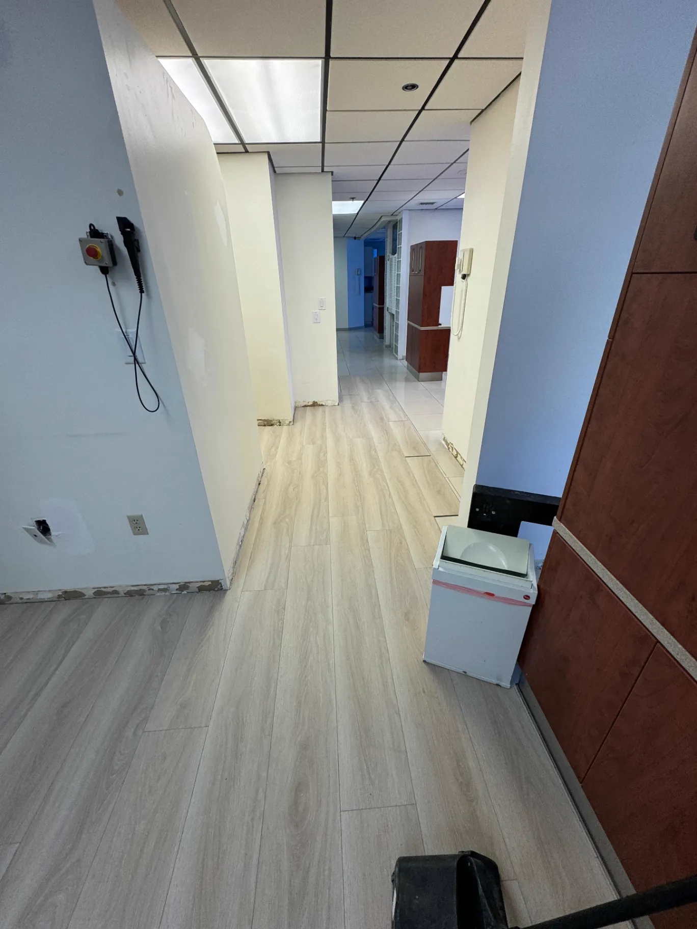 In-progress photo — dental office hallway in Miami during flooring installation by Colors Wood Floor Corp, with new wood-look planks meeting the remaining original tile.