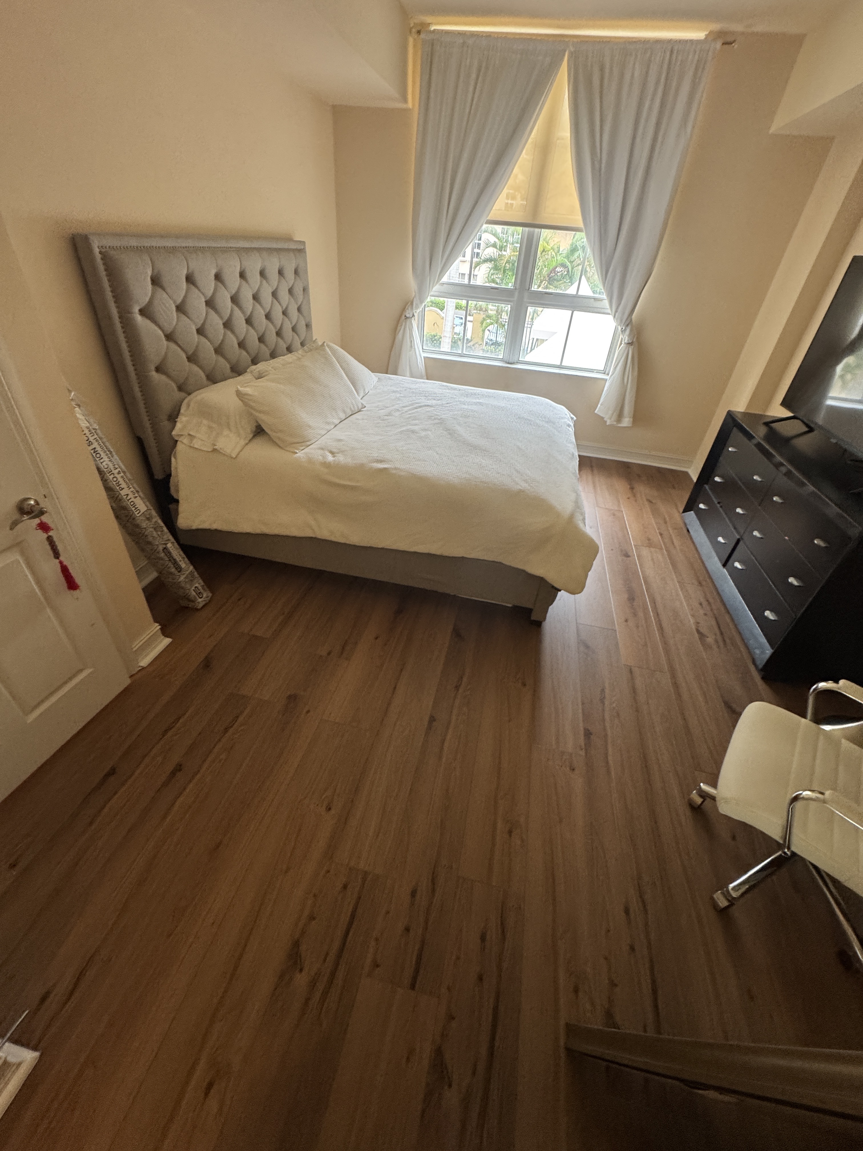 Completed vinyl wood-look flooring in a bedroom of an Aventura, FL condo, with the bed, dresser and window visible.