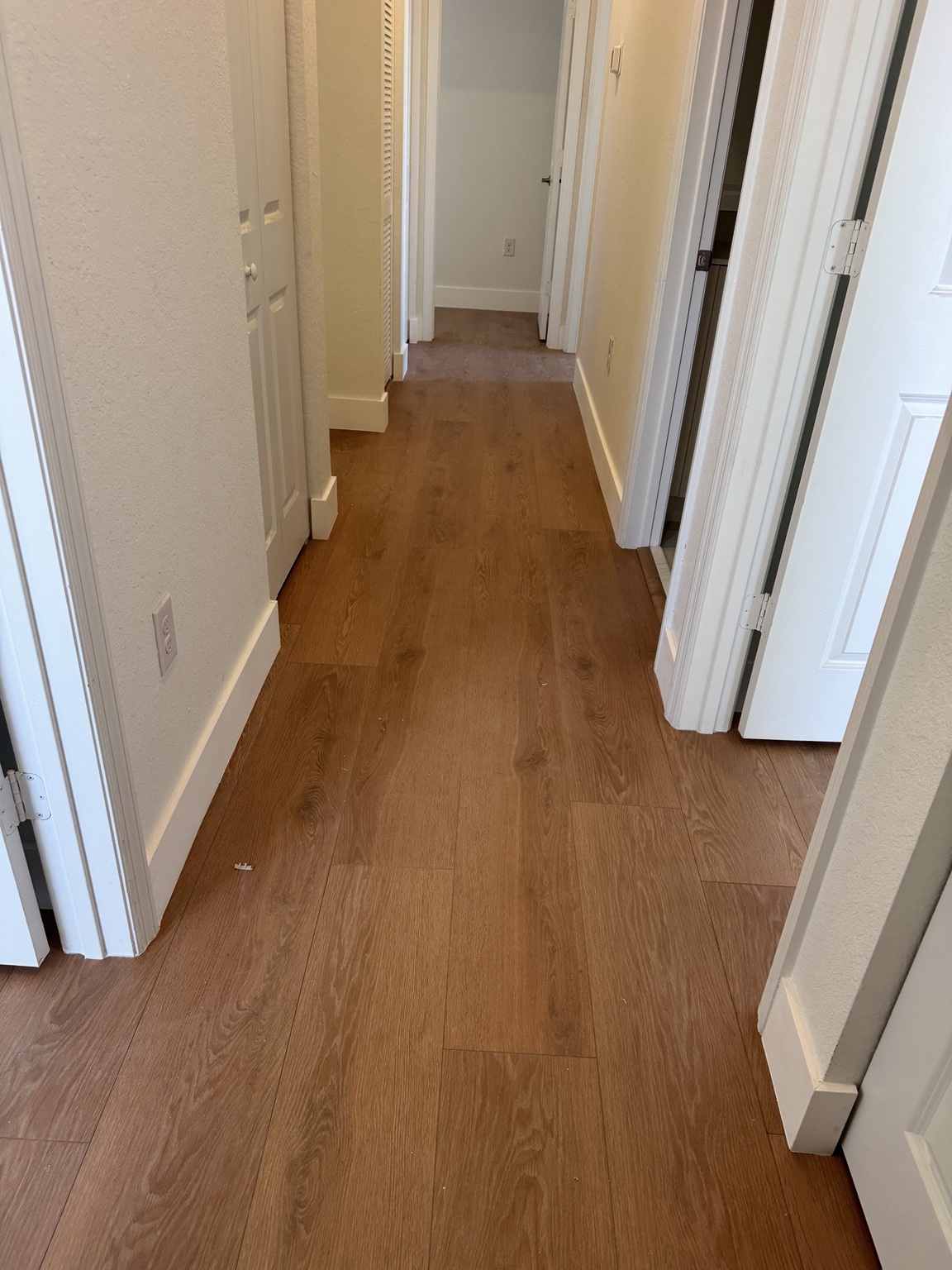 Finished residential hallway with warm oak laminate flooring and new white baseboards