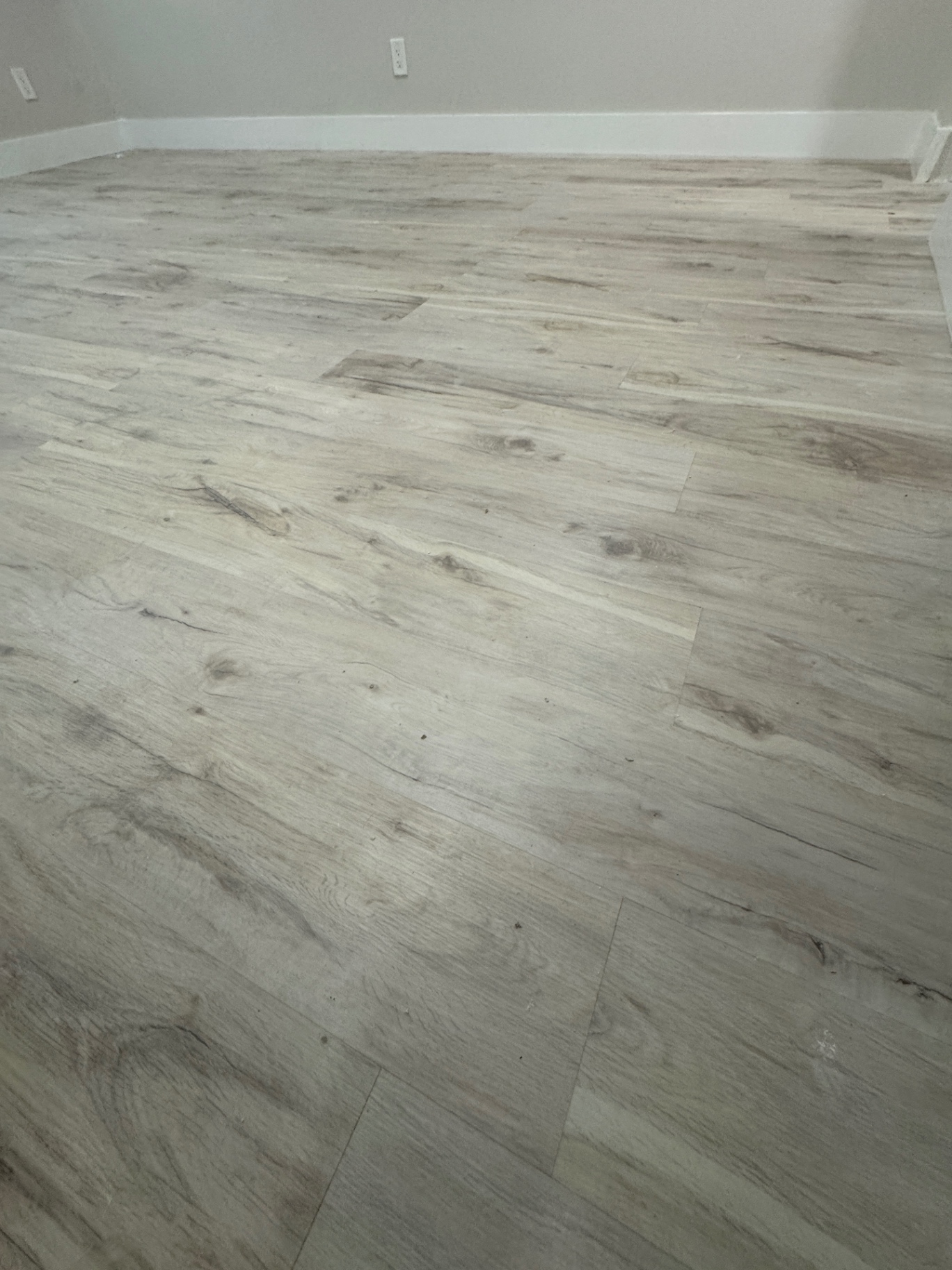 Completed flooring repair with light wood-look planks and white baseboards.