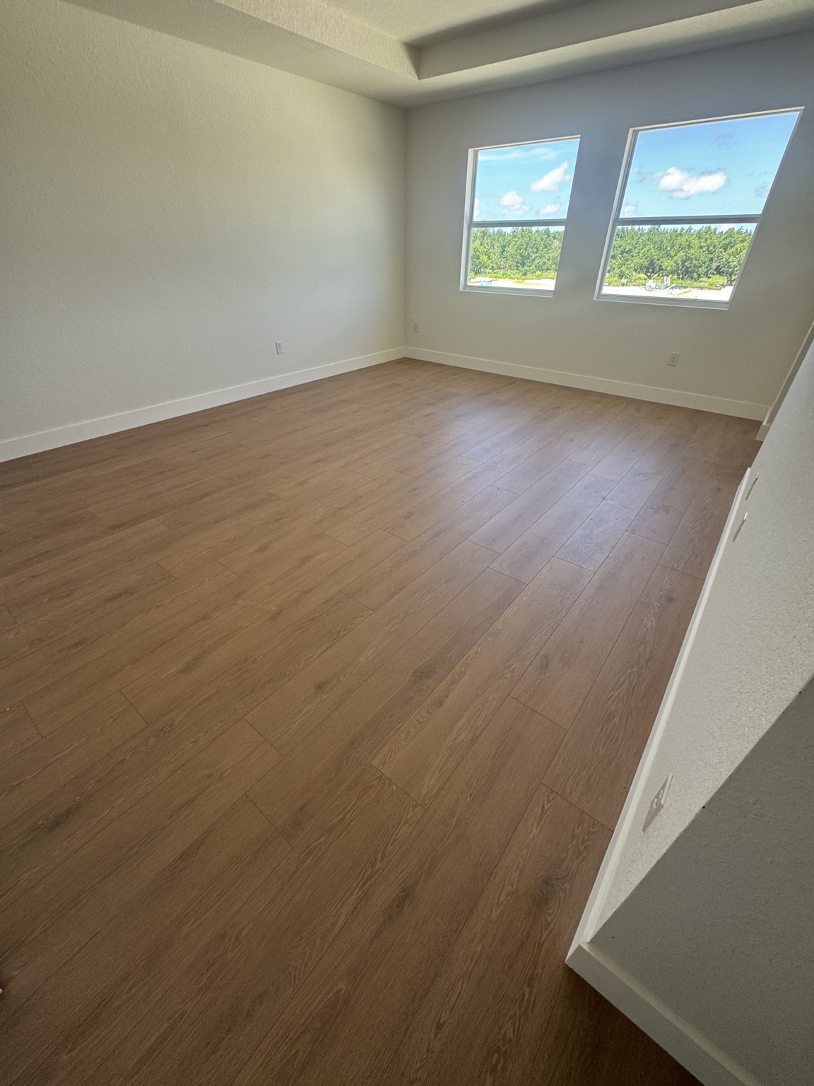 Finished bedroom with warm oak laminate flooring and white baseboards