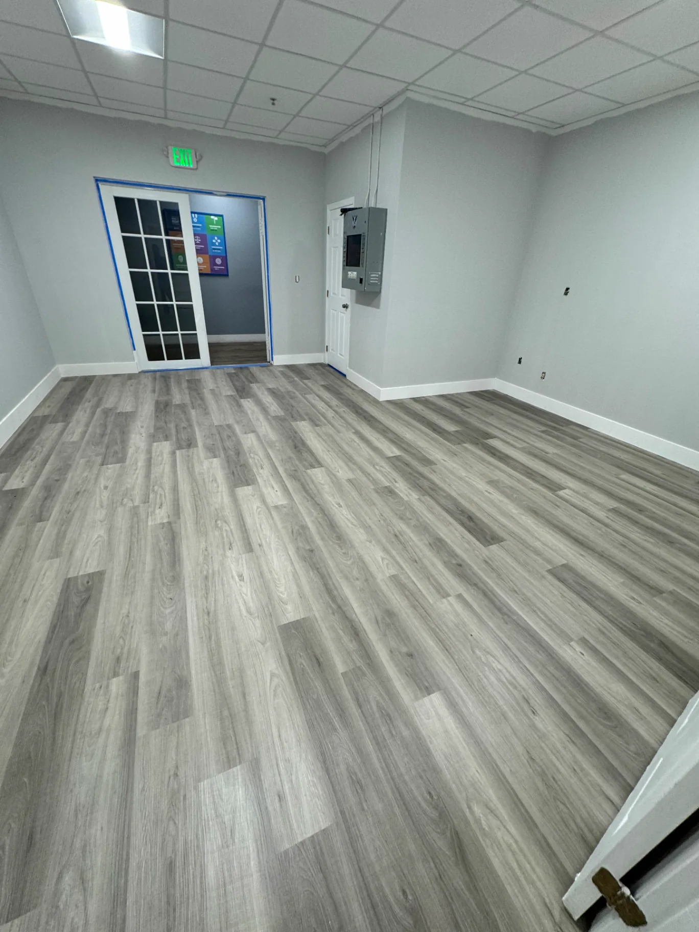 Miami office room with light gray wood-look flooring by Colors Wood Floor Corp — French doors and electrical panel installed by others.