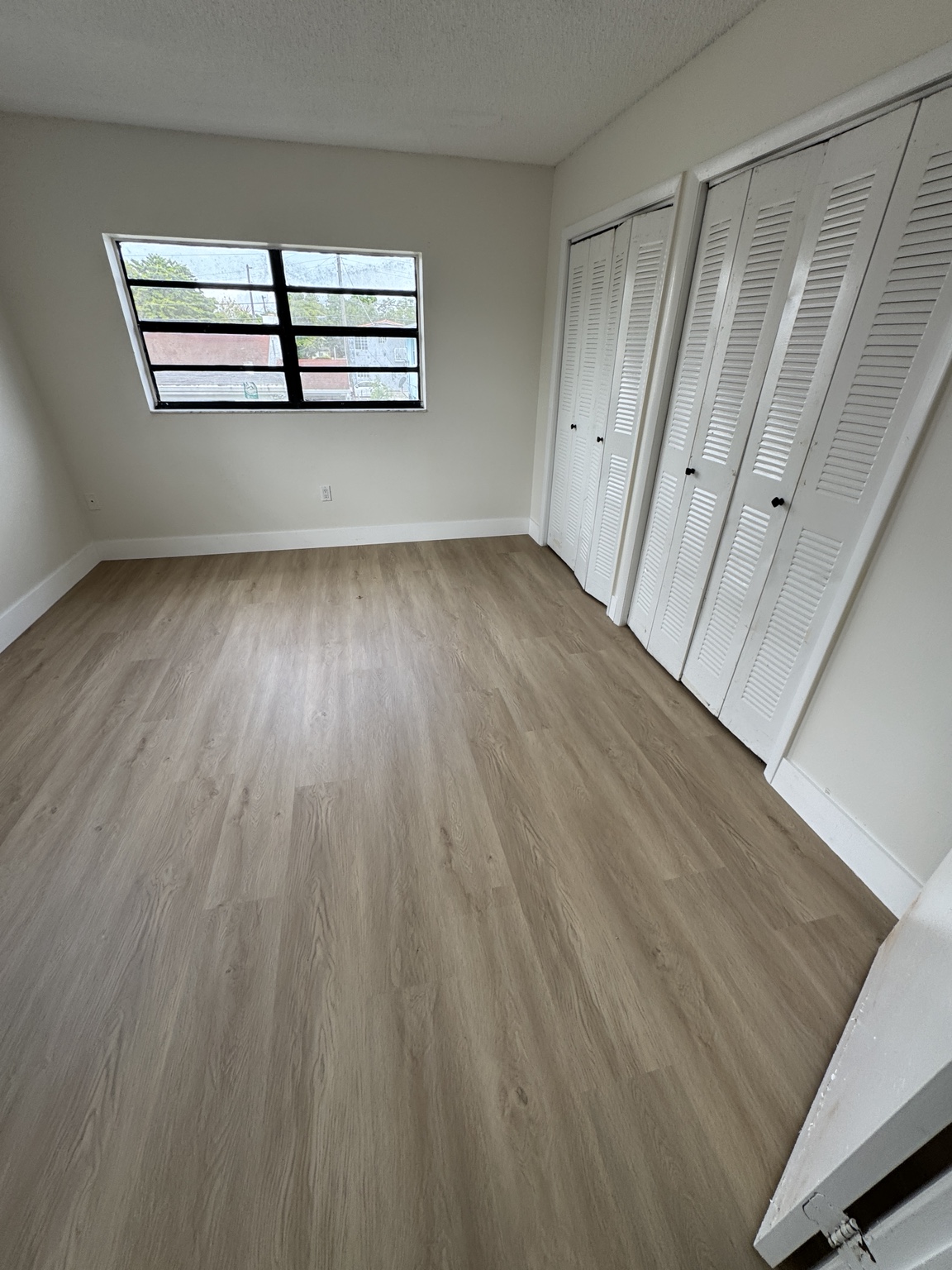 Bedroom after waterproof vinyl flooring installation with white baseboards.
