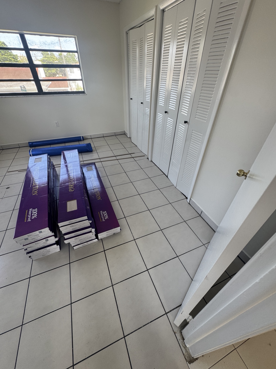 Bedroom before installation with light tile flooring and new waterproof flooring boxes staged on-site.