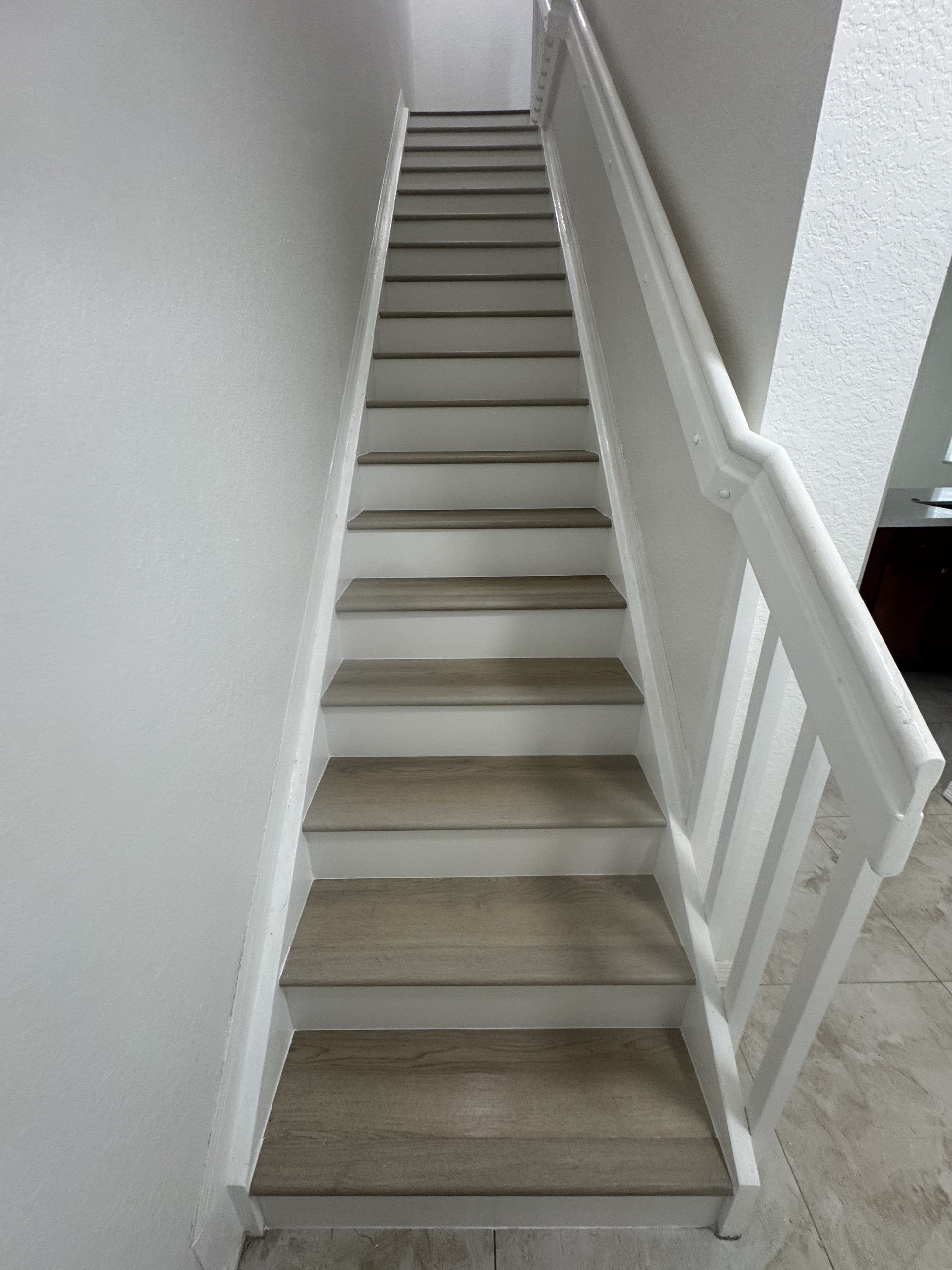 Staircase after new light vinyl LVP flooring installation with white risers, shot looking straight up the stairs