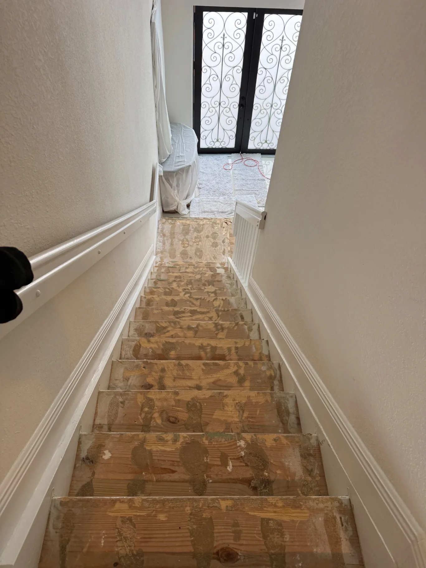 Existing staircase with previous surface removed — bare treads and adhesive residue, view looking down.