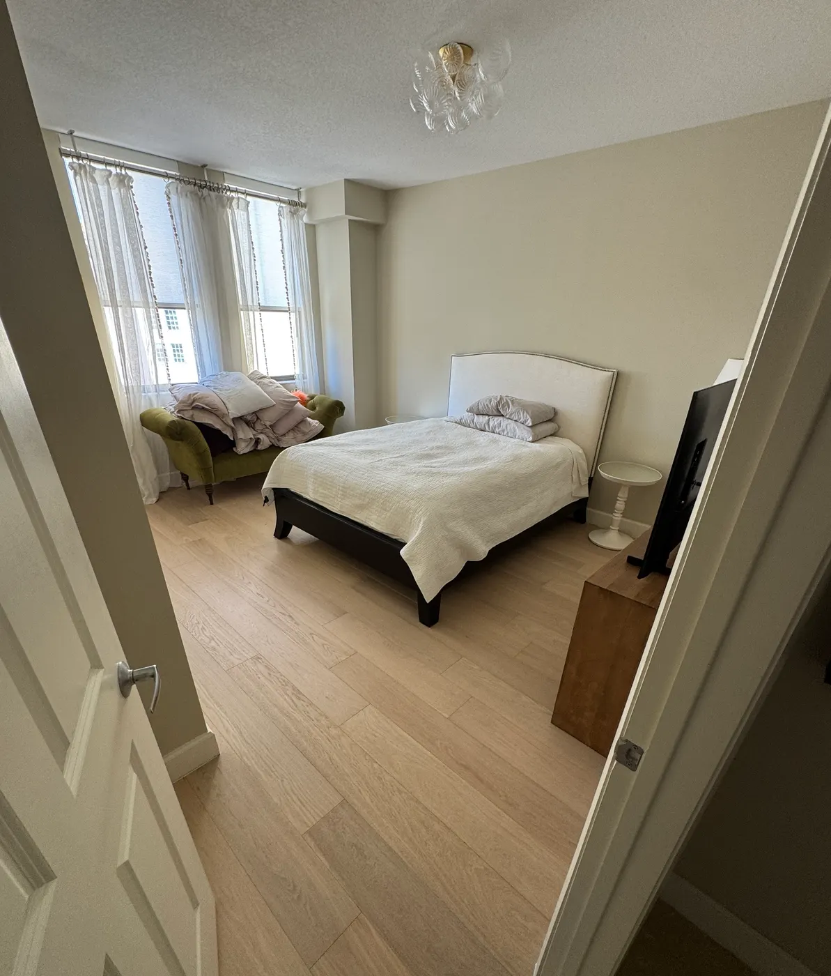 Bedroom seen from the doorway with new light-toned wide-plank flooring and white baseboards, installed by Colors Wood Floor