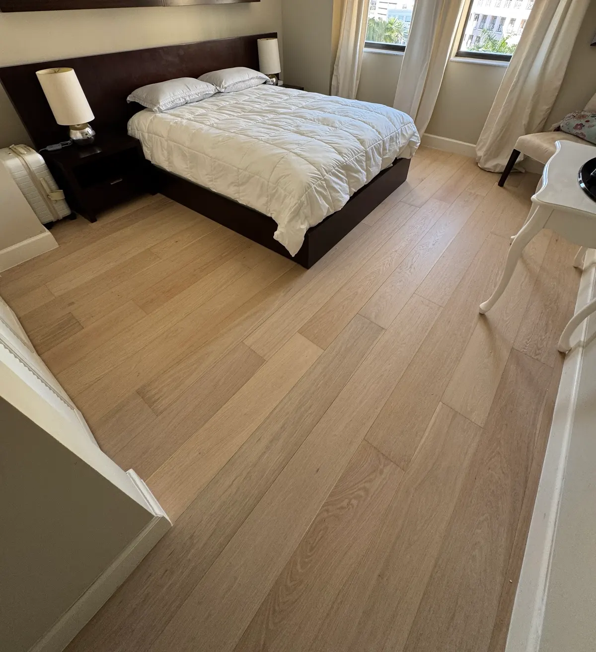Bright bedroom with new light-toned wide-plank flooring running toward the windows, installed by Colors Wood Floor