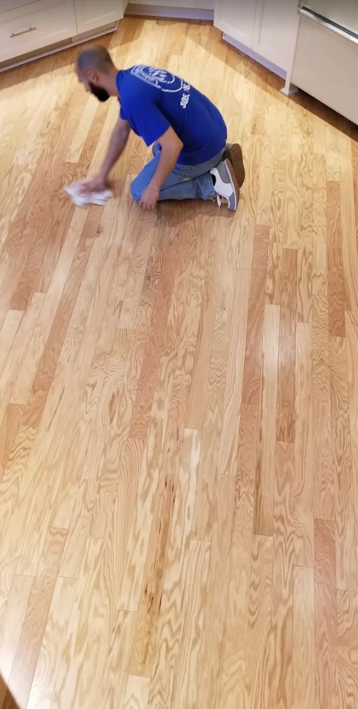 Colors Wood Floor installer in a company shirt wiping down a newly installed light-toned wood floor