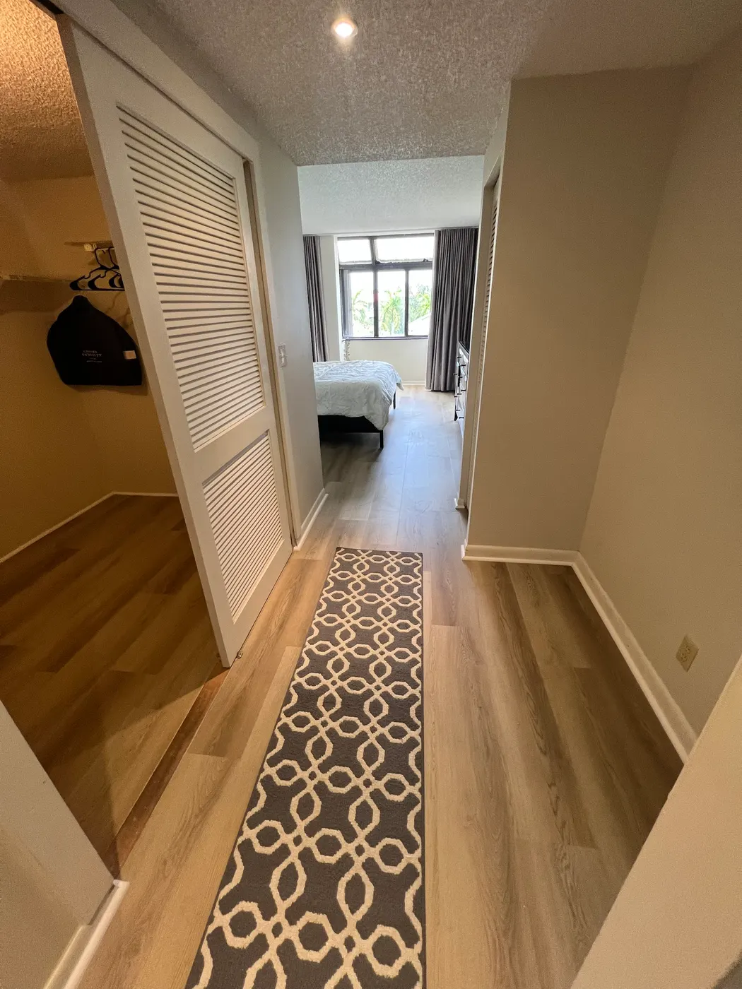 Hallway, closet and bedroom with one continuous wood-look plank floor and new white baseboards, installed by Colors Wood Floor