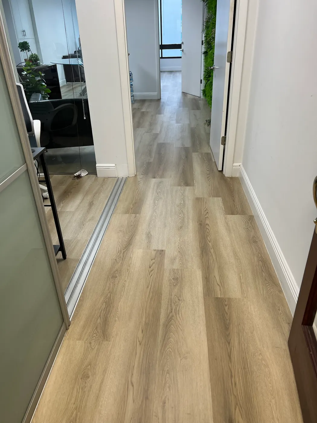 Office hallway with new light wood-look plank flooring running into the private offices, finished with white baseboards, installed by Colors Wood Floor