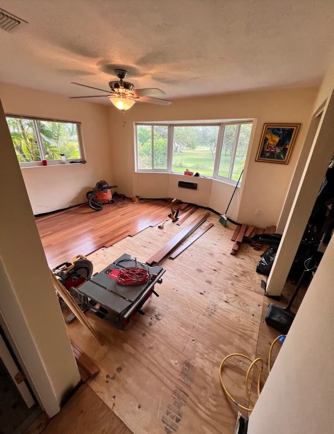 Wood flooring being installed over a new plywood subfloor, with installation tools in the room